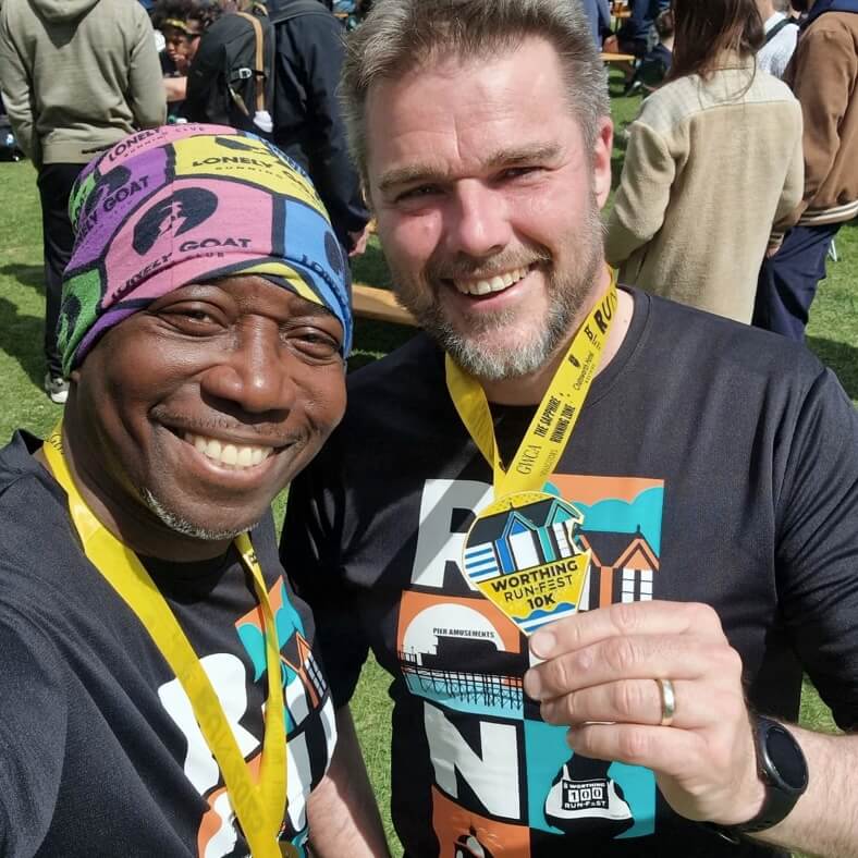 Two men, Tee and Simon, with medals and running race tee shorts, smile after the Worthing Runfest 10K in May 2025